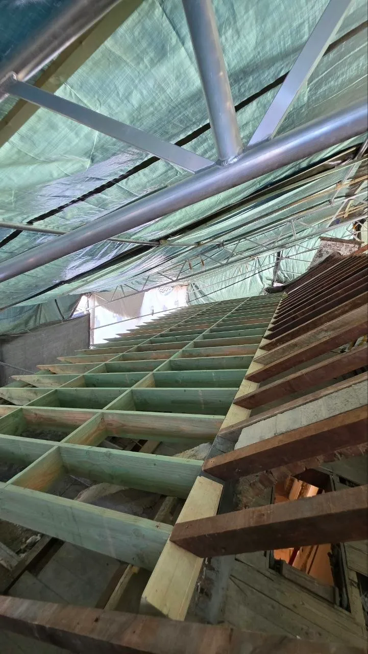 Zicht van onder het tijdelijk dak: een nieuwe houten dakconstructie wordt droog opgebouwd onder het zeil
